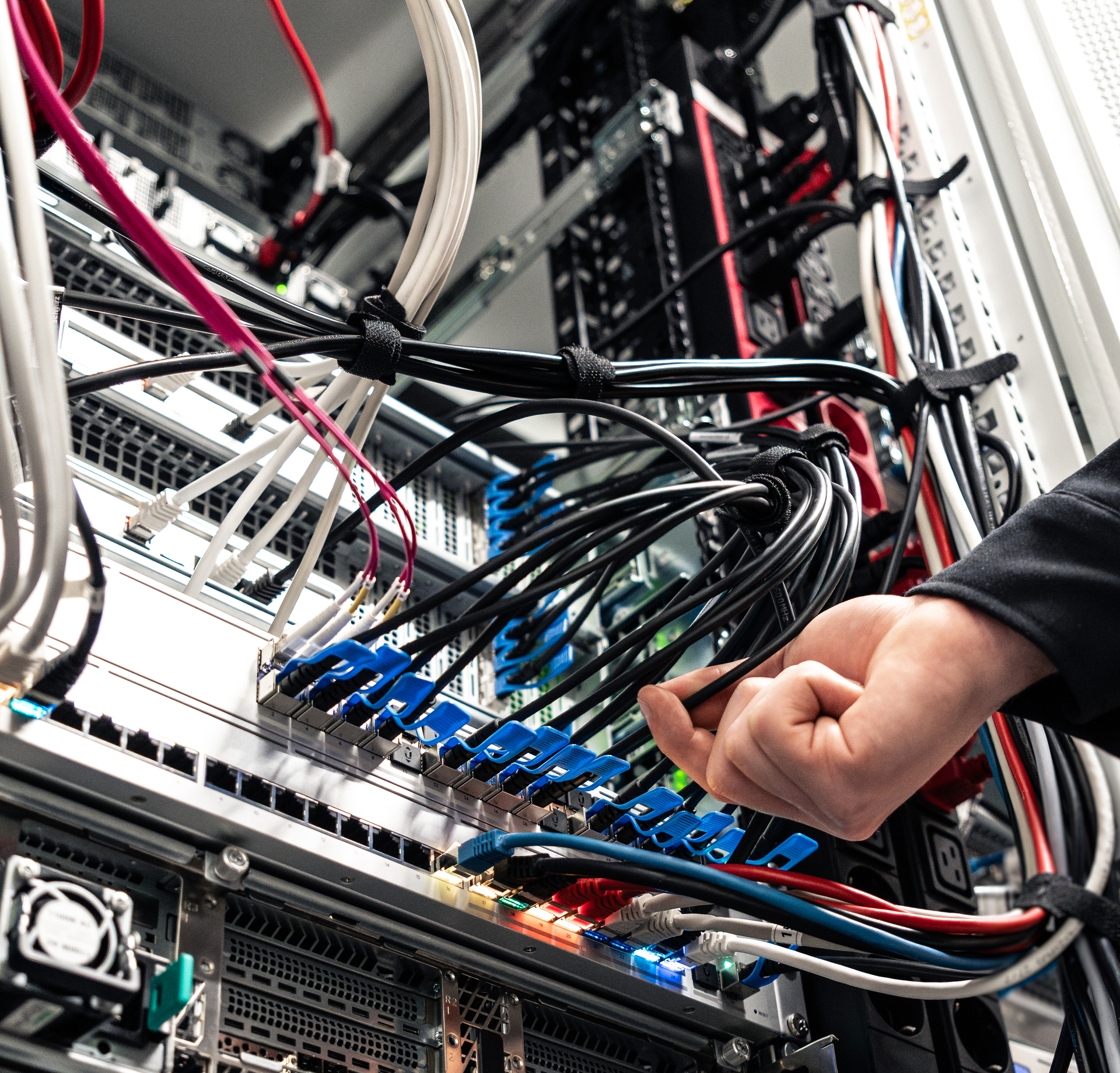 Hand eines Mitarbeiters an der Verkabelung eines Serverschranks